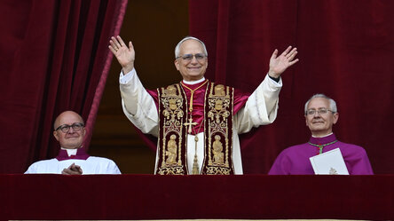 Ein grauhaariger Mann im weißen Papstgewand mit rot-goldener Stola winkt